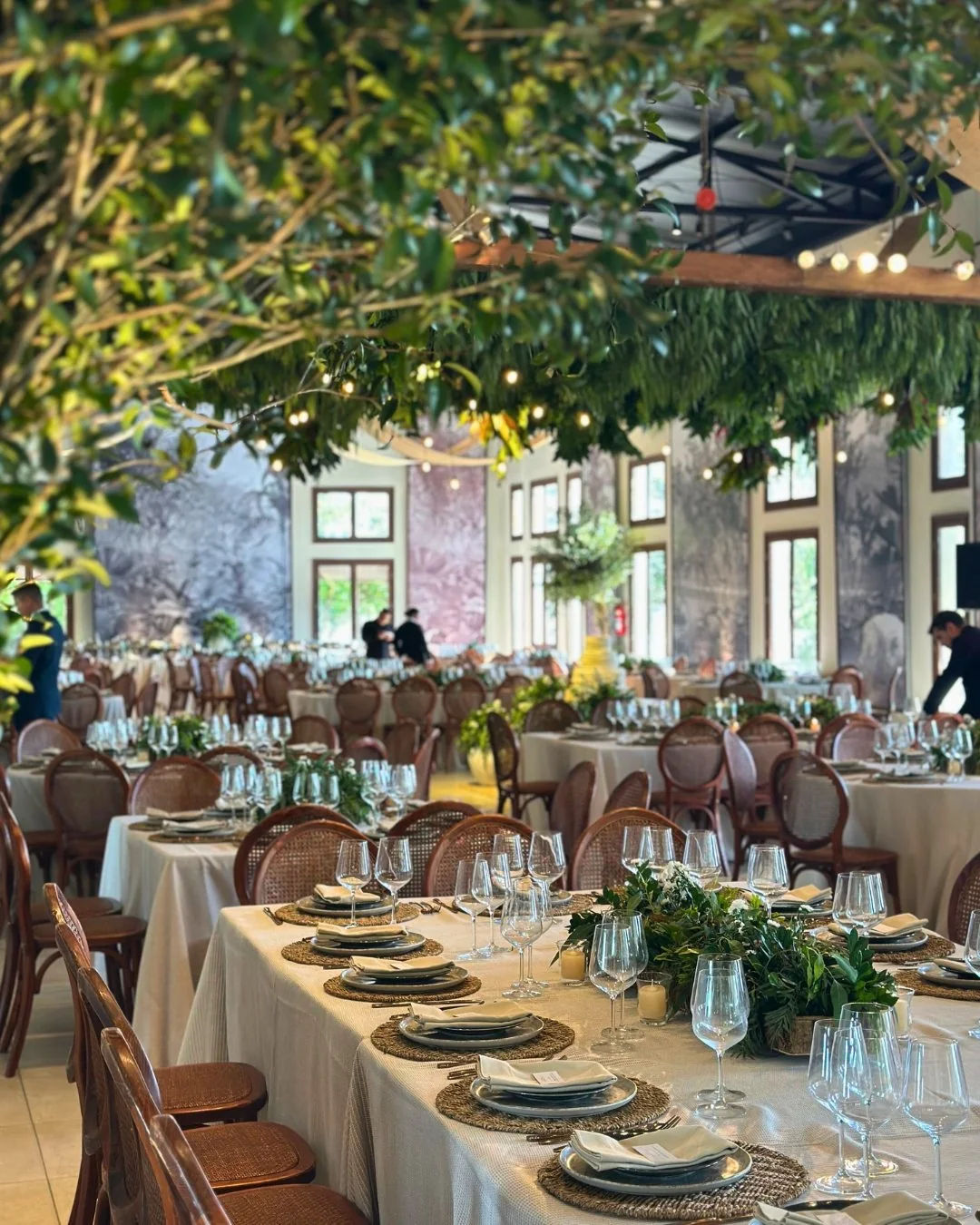 Decoración de evento social: salón con vegetación colgante y mesas largas